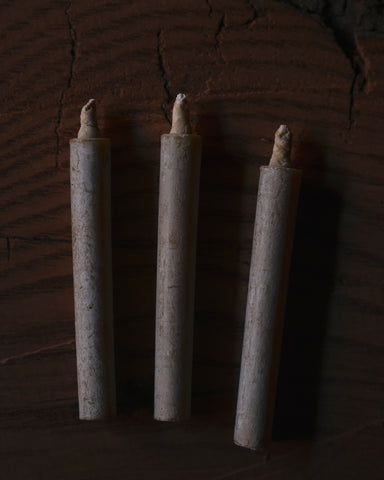 Three cylindrical candles with wicks on a dark textured background