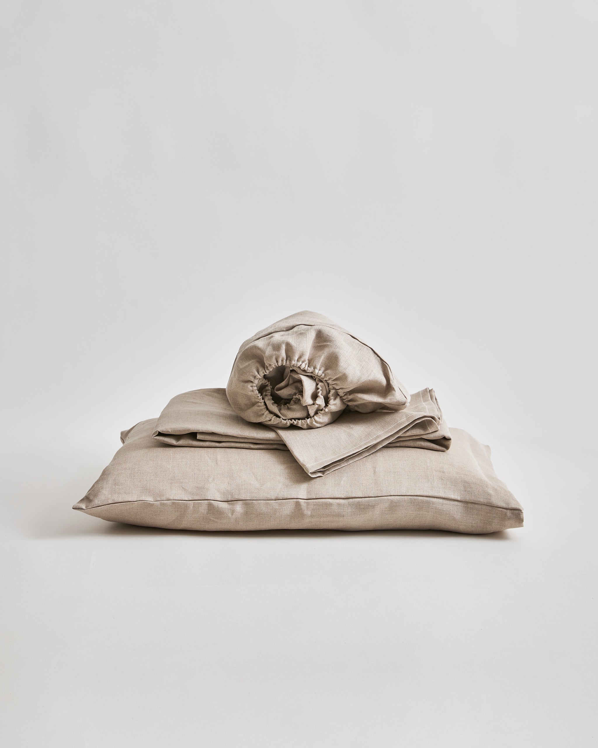 Stack of unbleached linen folded sheets on a pillow by Iwata on a gray 
