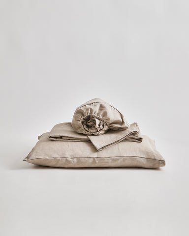 Stack of unbleached linen folded sheets on a pillow by Iwata on a gray 
