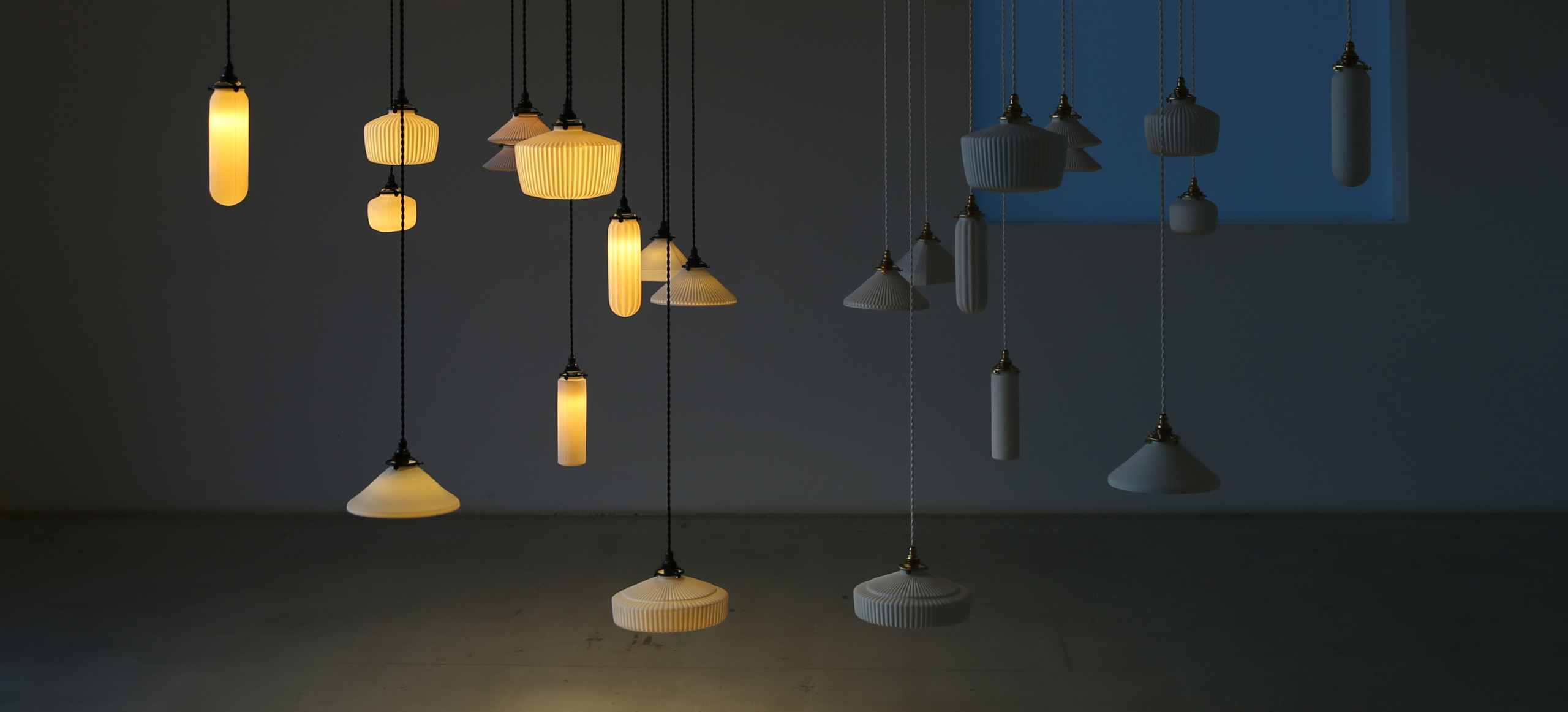 Many porcelain hanging pendants of various shapes and sizes on display in a room. Half of them on the left are lit. The other half are not.