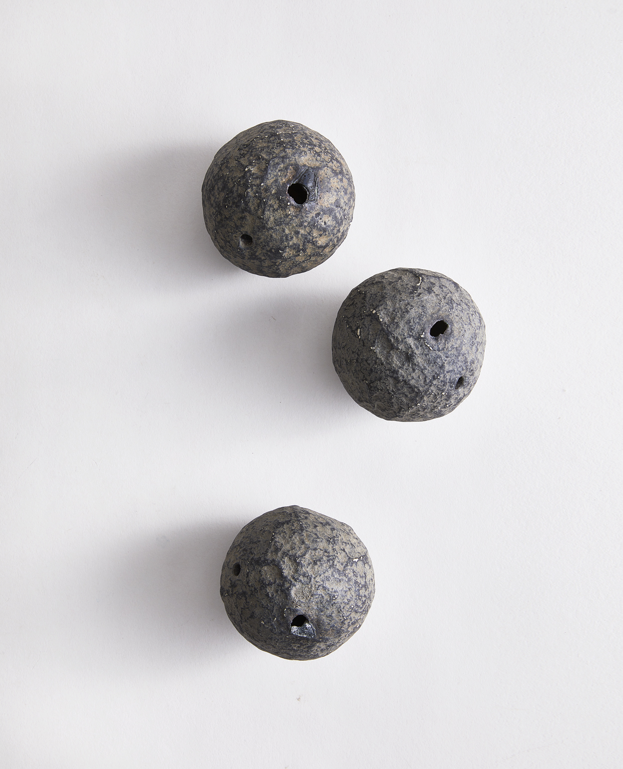 Three spherical wall hanging vases by Keisuke Iwata scattered on a gray background