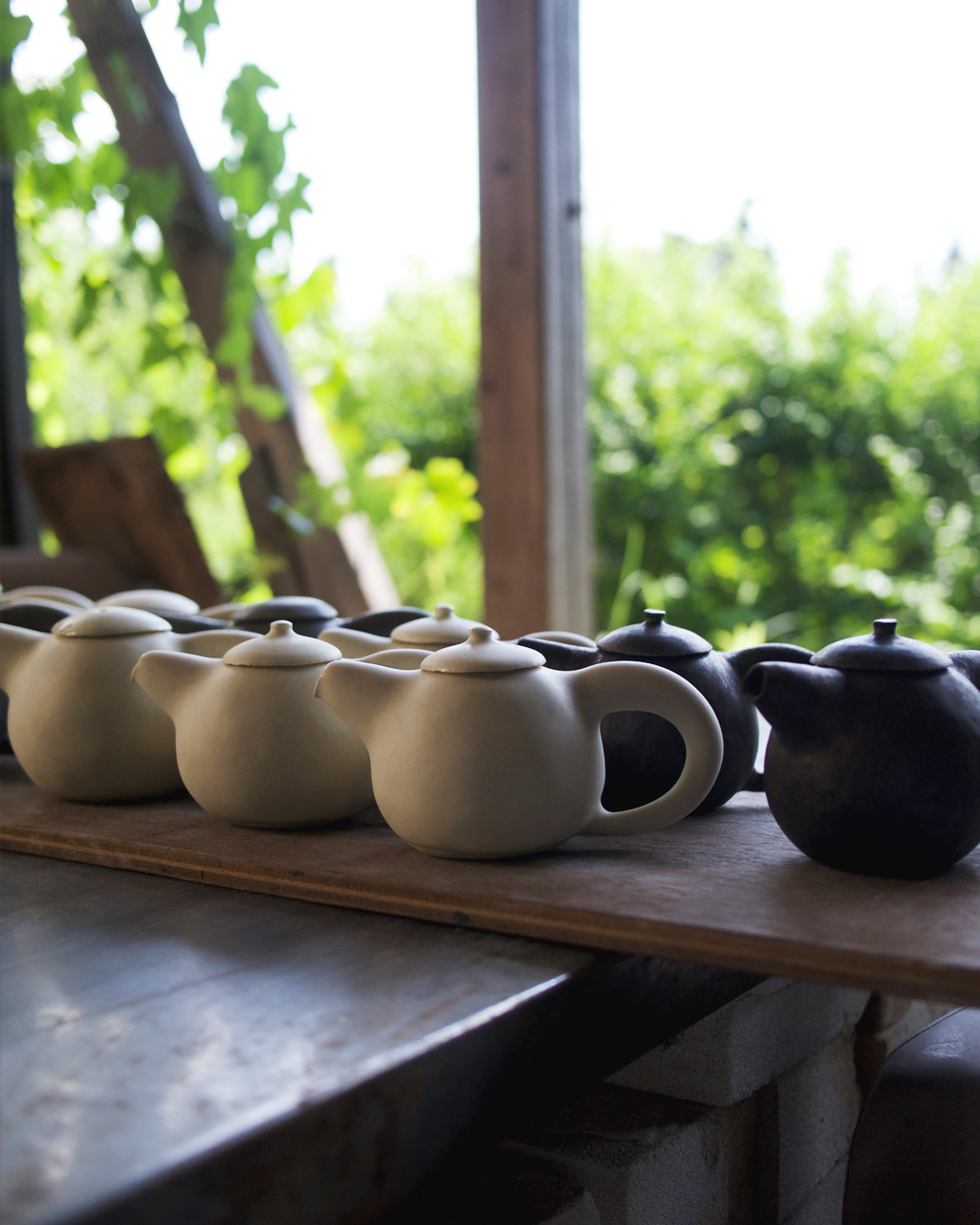 Close up view of a white ceramic signature keisuke Iwata teapot against a green treelined backdrop