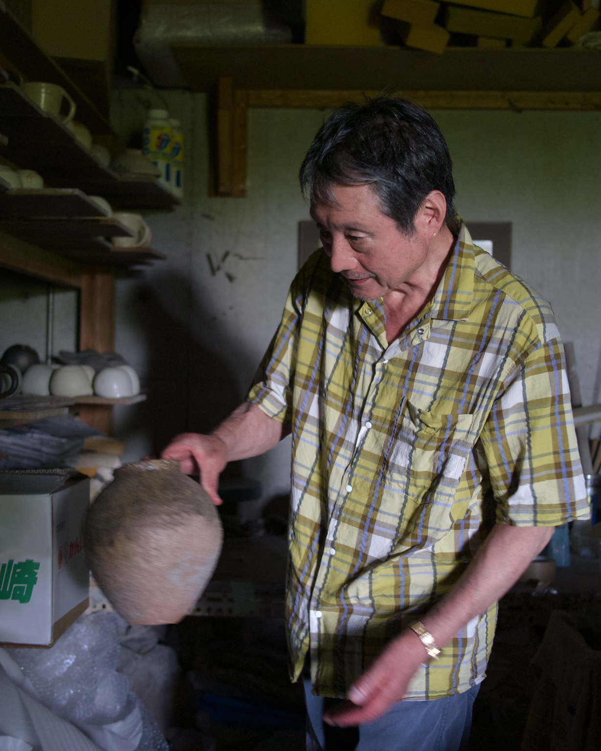 Keisuke Iwata holding an anagama woodfired vase picked up from the shelves covered with ceramics at his studio