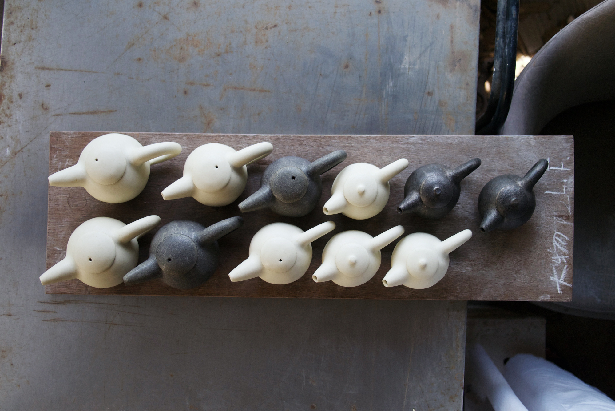 Ceramic black and beige/white teapots from top view resting on an old wooden plank after just being fired