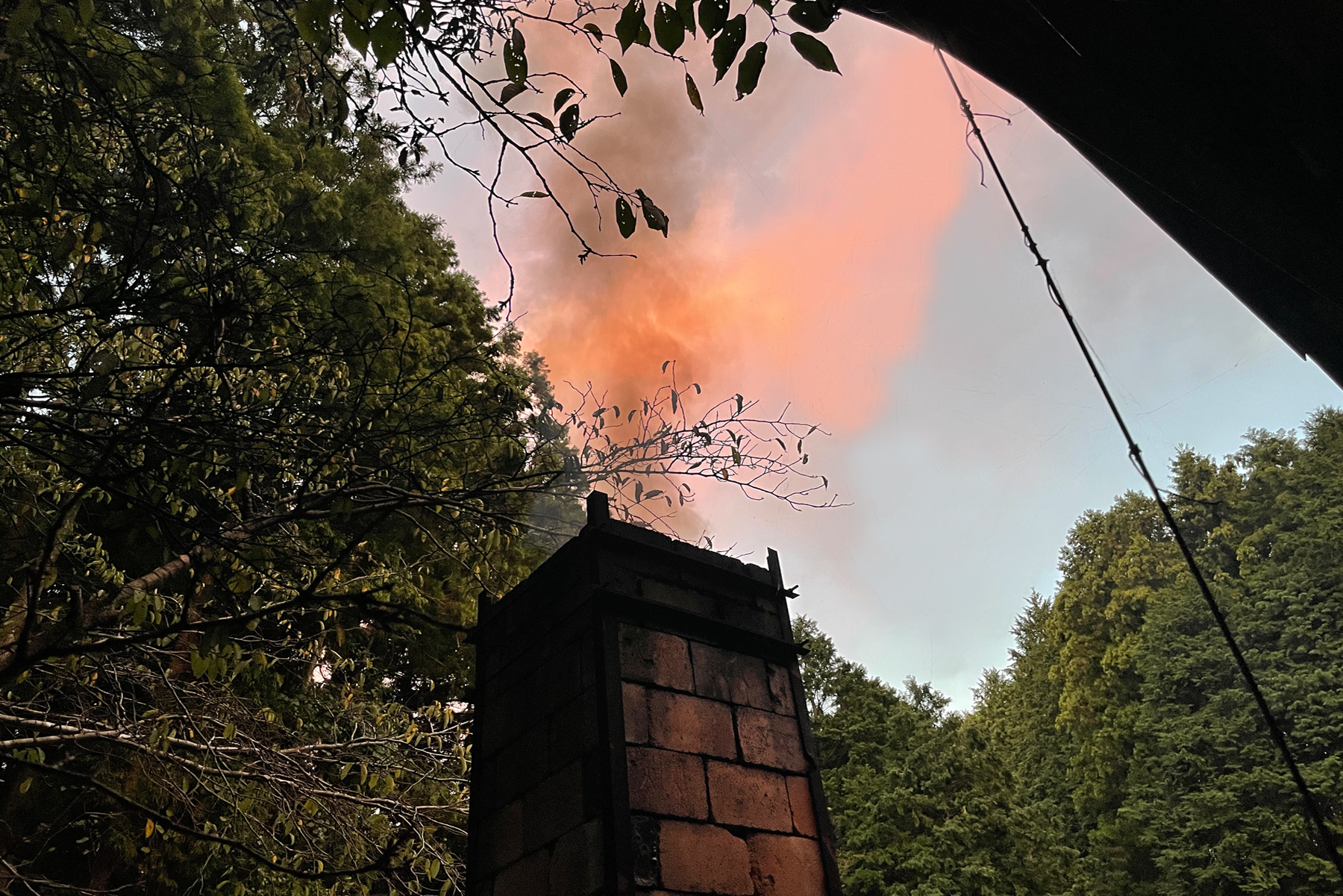 chimney from the anagama kiln with pink smoke against light blue skies