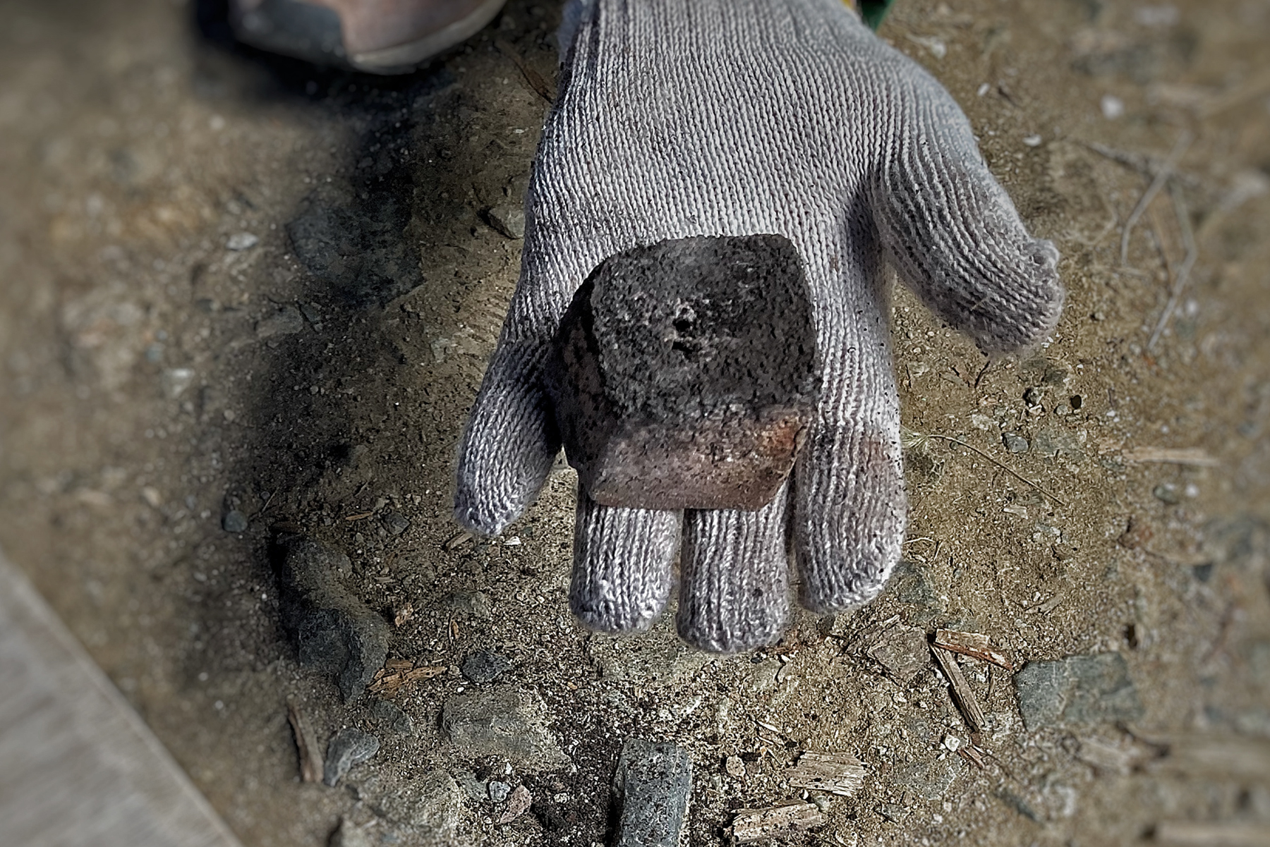 A gloved hand of Keisuke Iwata's holding an ashen stone cube vase that just came out of the anagama kiln