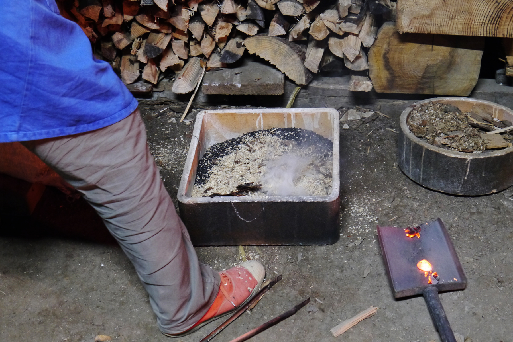 Keisuke Iwata beside a pit of sand and sawdust with a shovel to remove a hot anagama piece out of the kiln