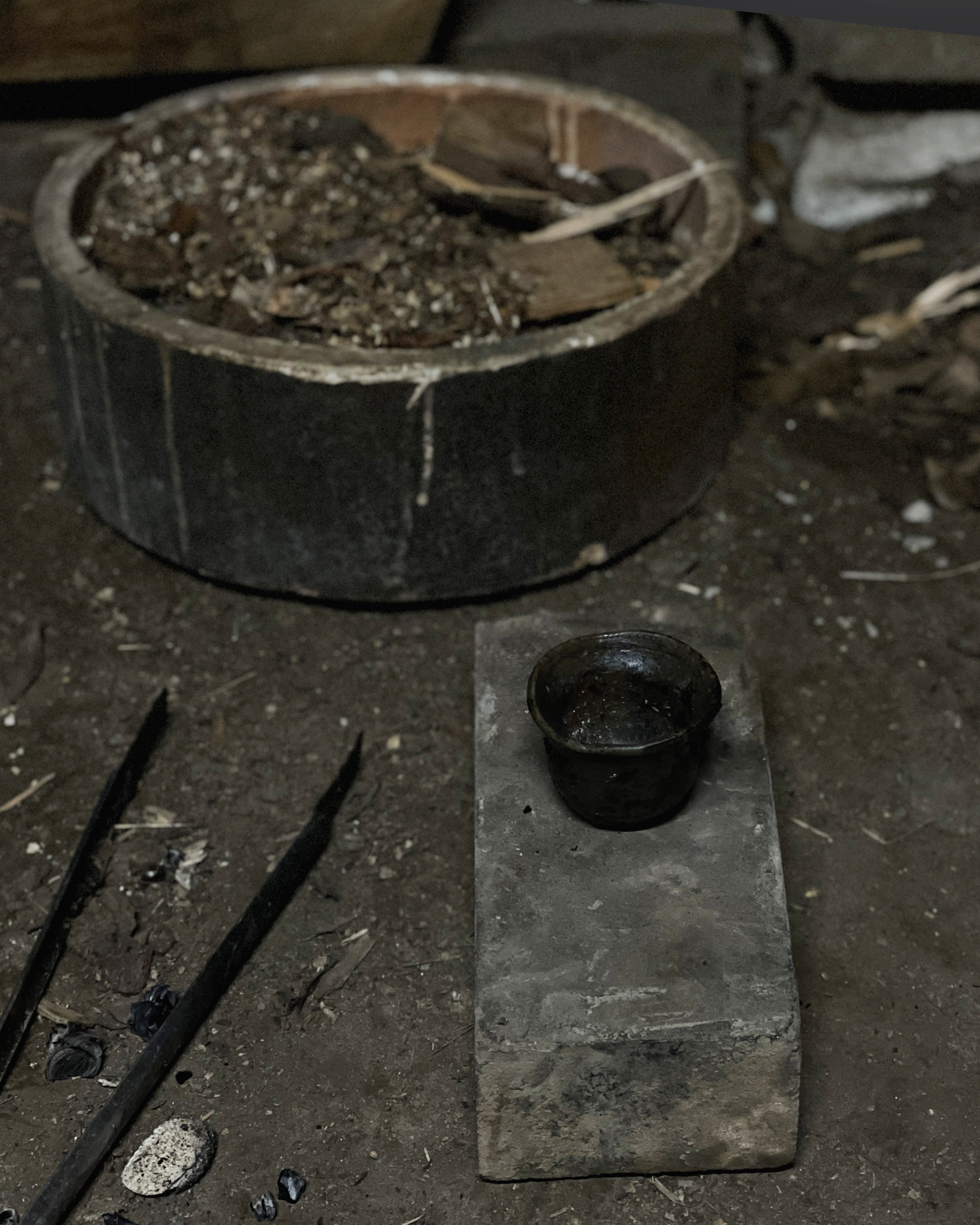 A black anagama cup just removed from the kiln resting on the ground on top of a plank of wood