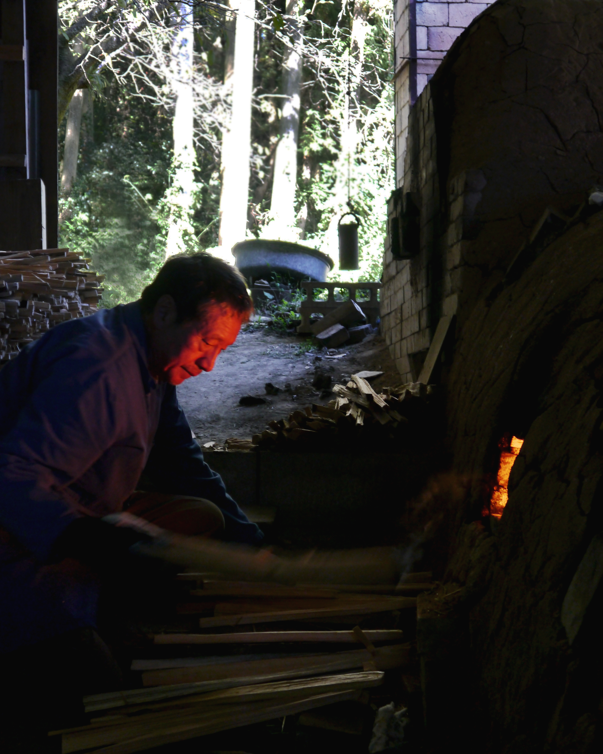 Keisuke Iwata's face glowing red as he looks into the flames from the opening of the anagama kiln