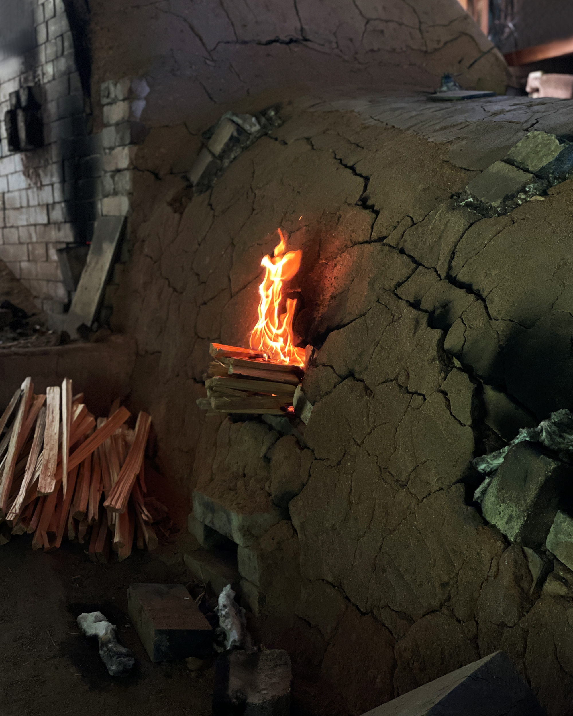 Pine wood fire logs and orange fire flames coming out of a small hole on the side of the anagama kiln
