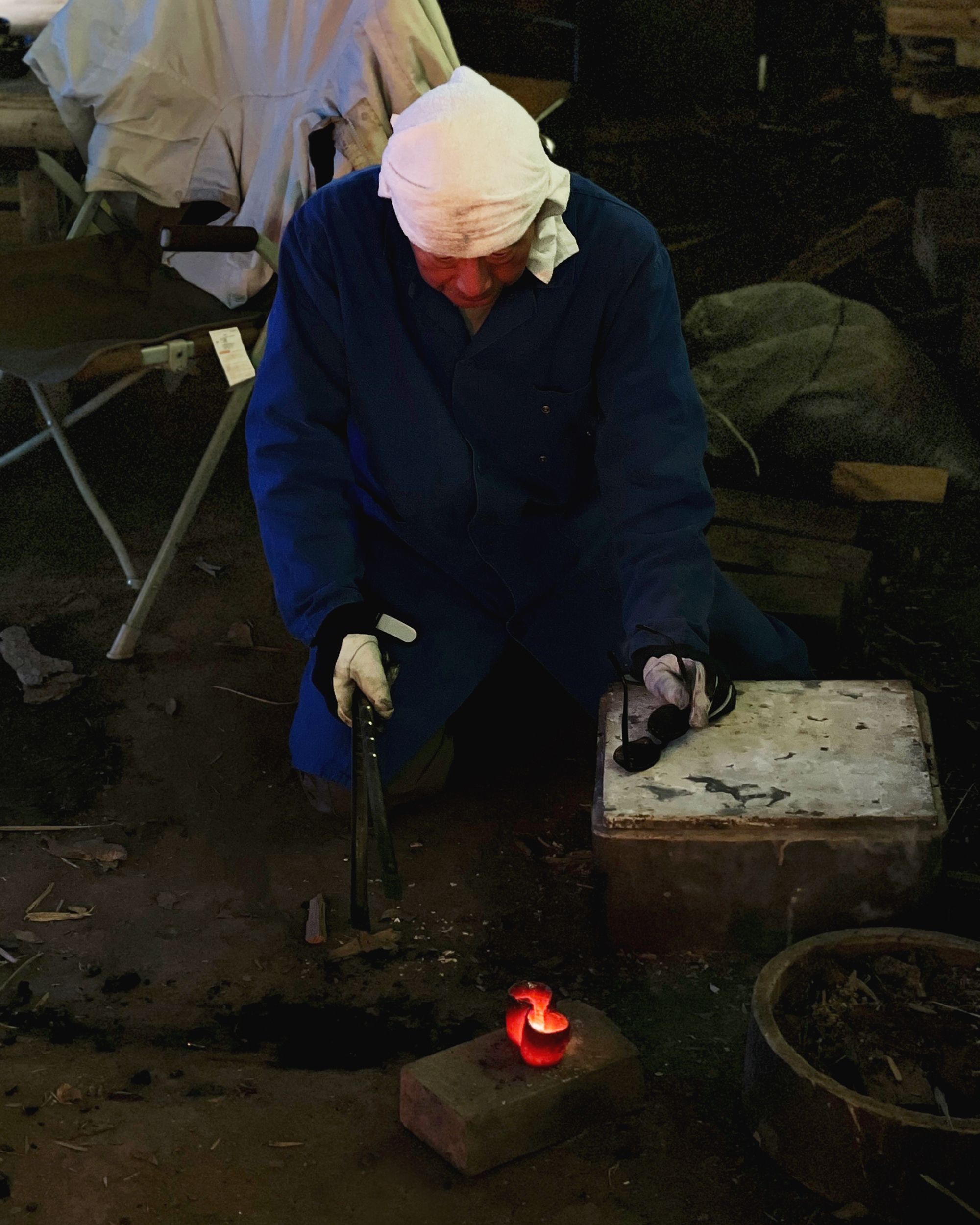 Keisuke Iwata with towel on head looking down at a red ember teacup just removed from the anagama kiln