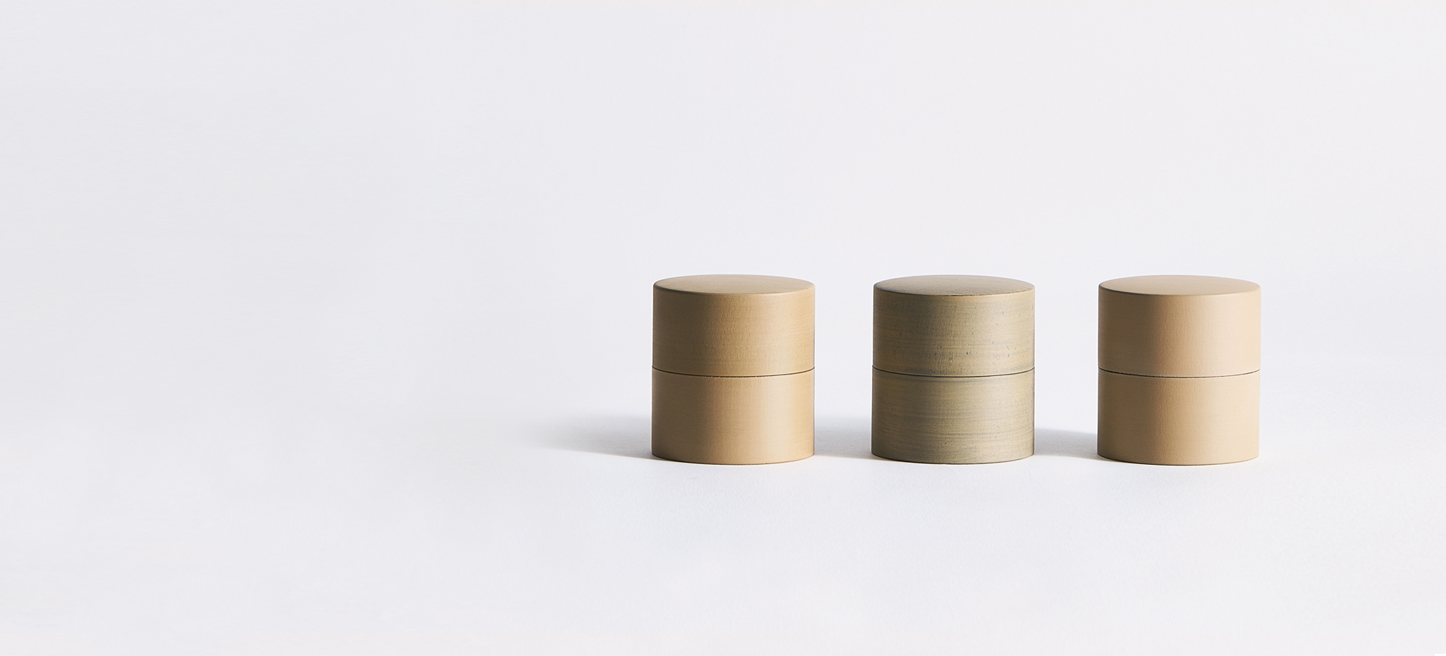 Three beige-toned tea canisters by Ryuji Mitanilined up on a gray background