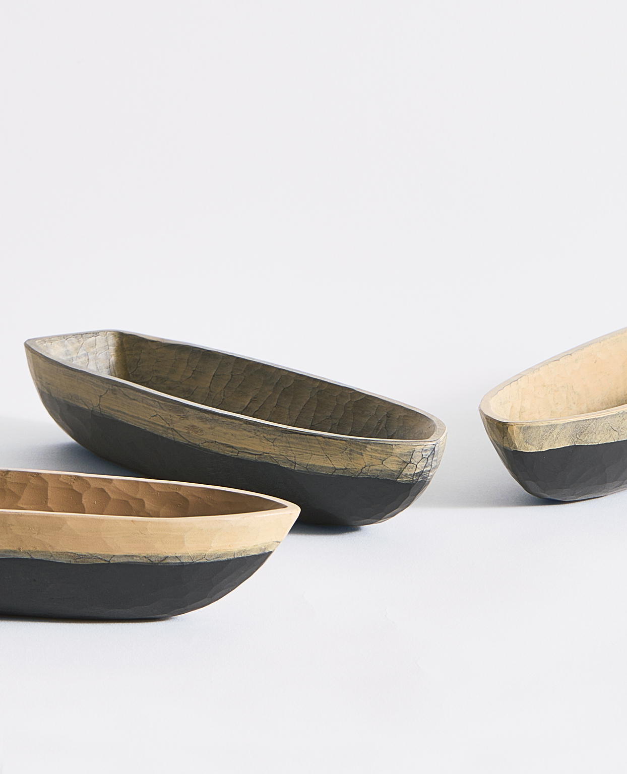 Cropped image of three stationary boat bowls in a black bottom exterior and different beige toned interiors on a gray backgound