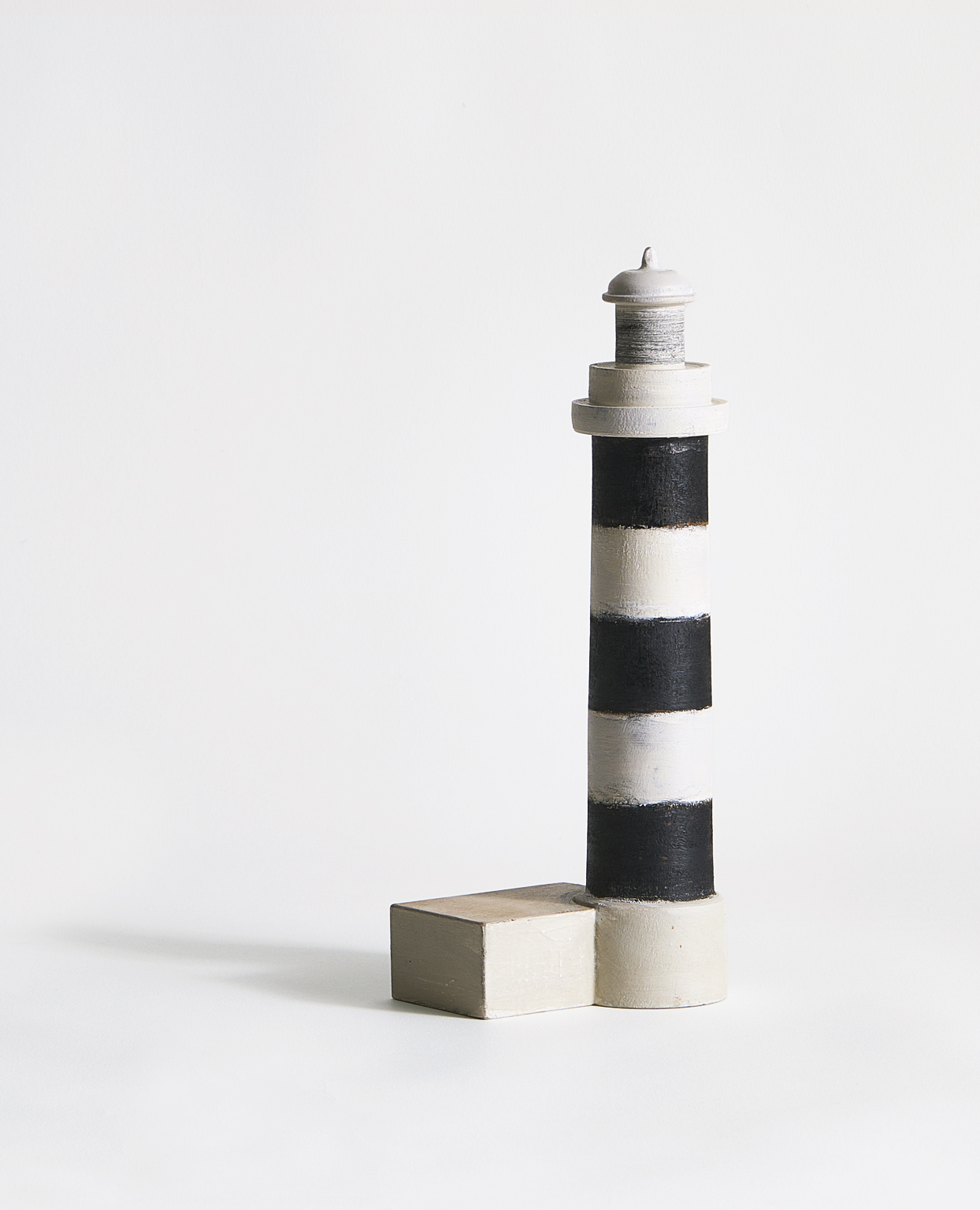 Sculptural artwork of a wooden lighthouse featuring black and white stripes by Ryuji Mitani on a gray background