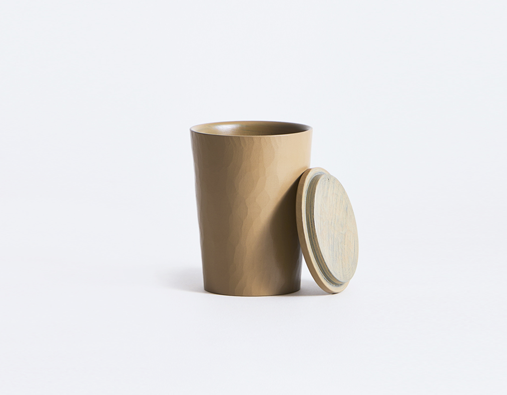 Beige coffee cup with lid leaning on the right side by Ryuji Mitani on a gray background