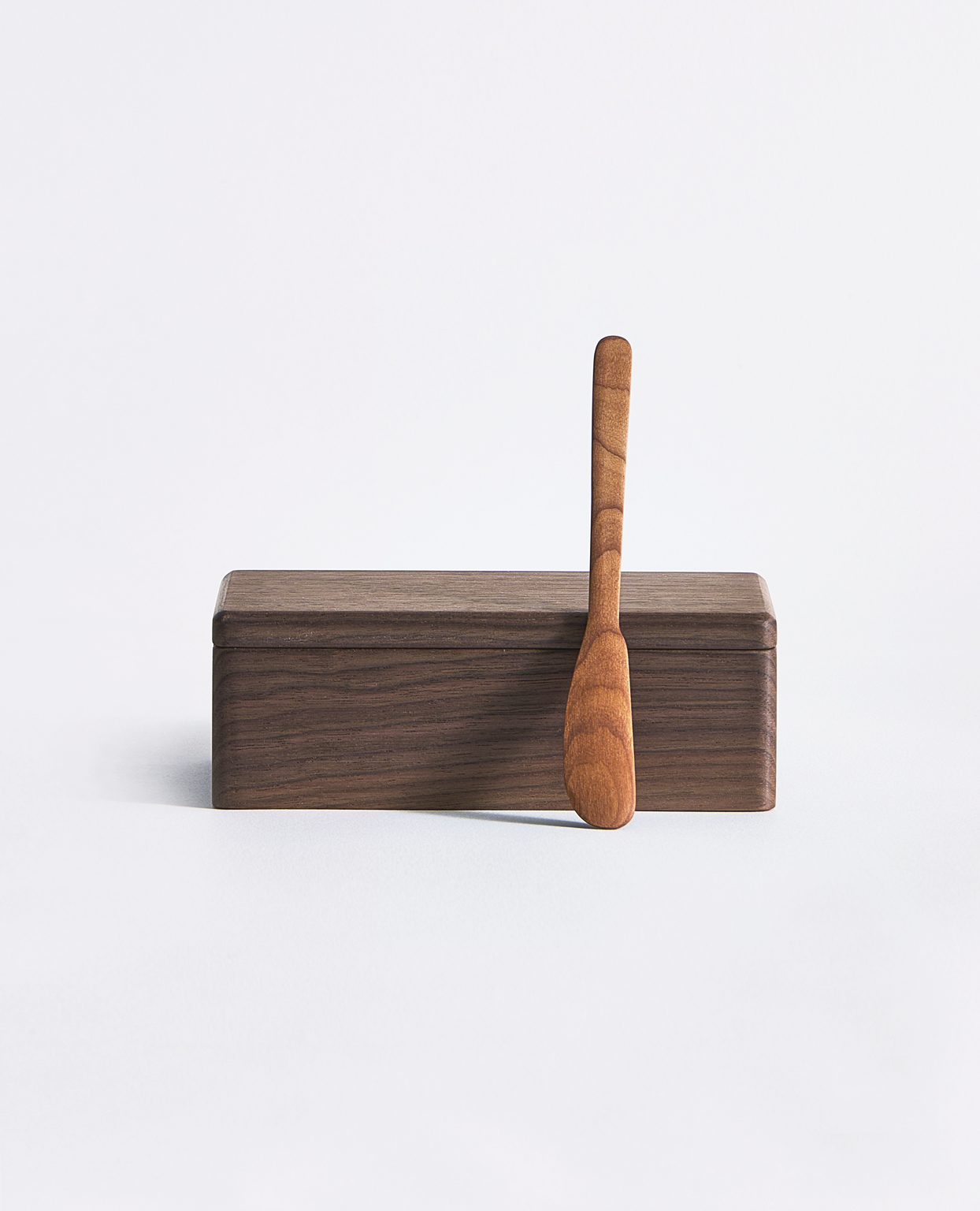Dark brown butter box with warm brown spoon laid leaning in front of box by Ryuji mitani on a gray background