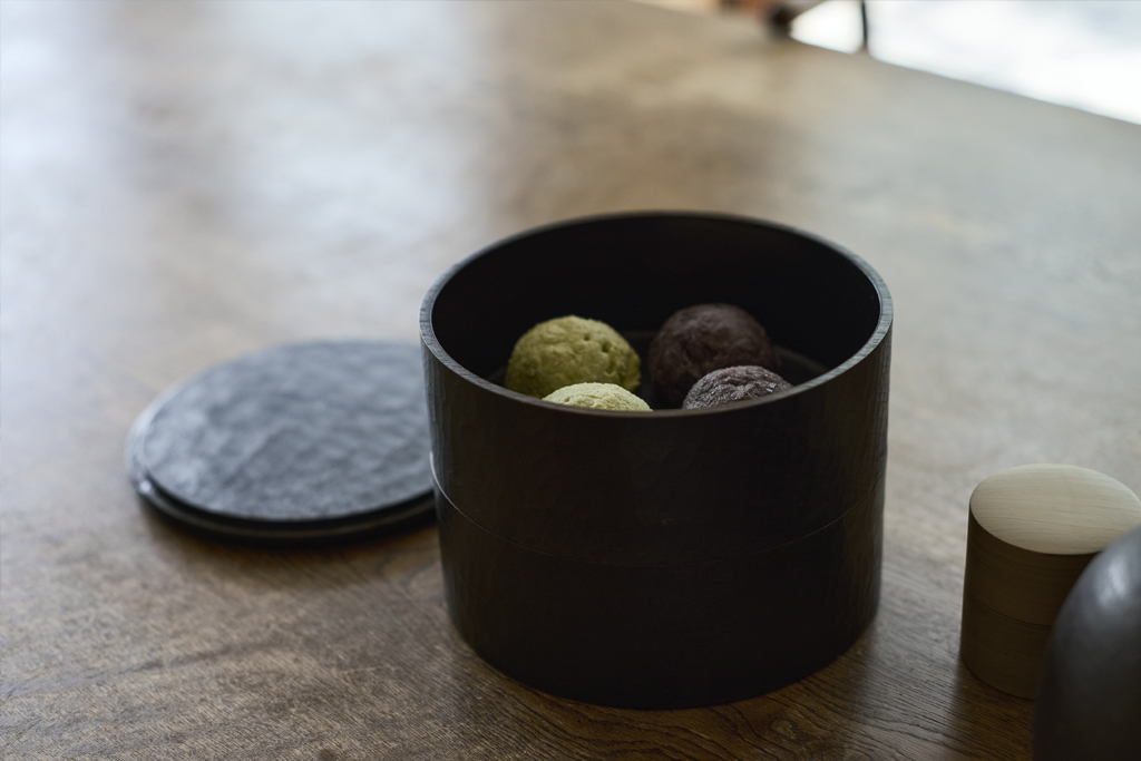 Two-tiered black opened wooden box on a wooden table, displaying sweets inside.