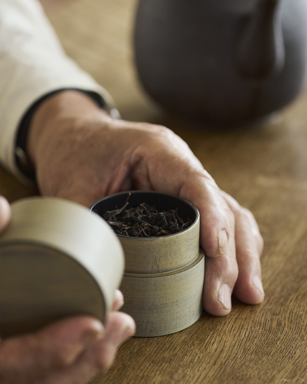 Hand holding an open Tea Case Usuzumi with a beige exterior and black interior made by Ryuji Mitani with tea leaves seen inside of it
