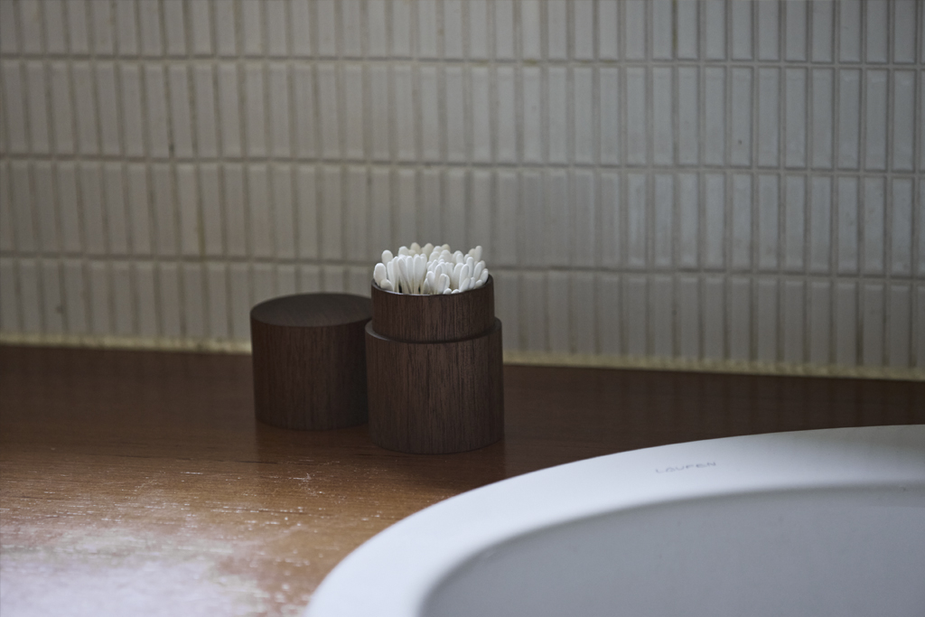An open wooden cotton swab container by Ryuji Mitani in a bathroom counter top next to a sink