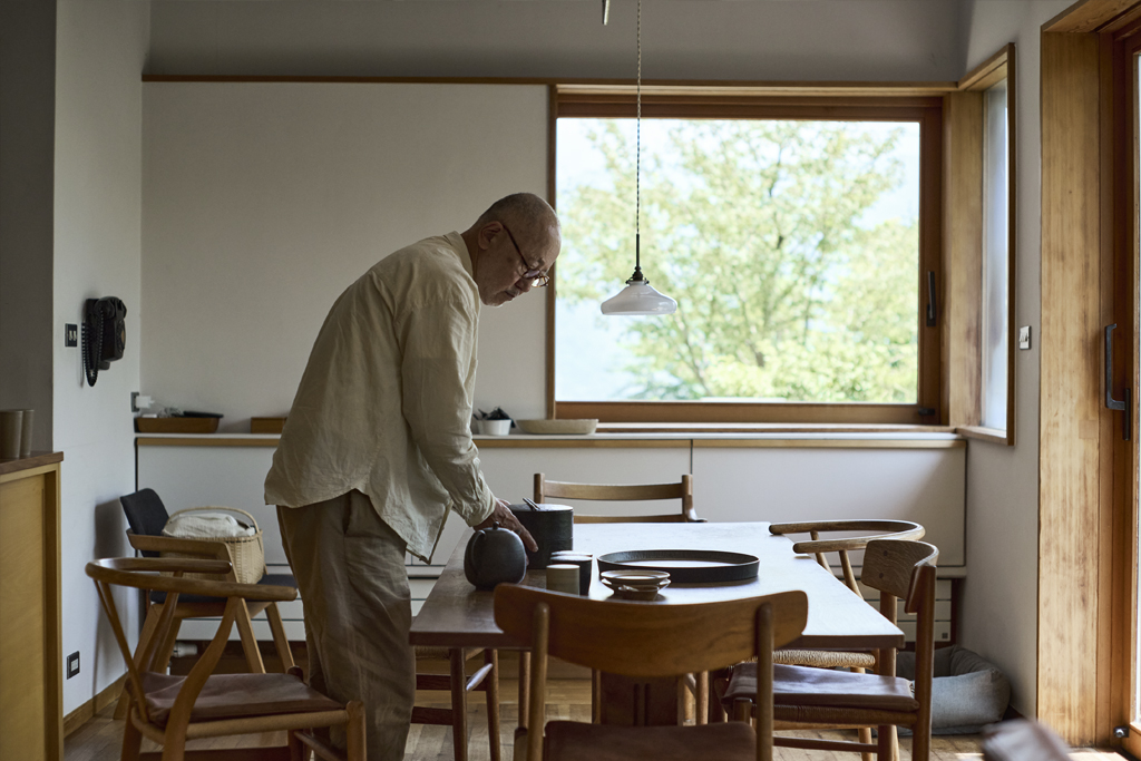 Ryuiji Mitani in his dining room placing wooden objects made by himself on a wooden table.