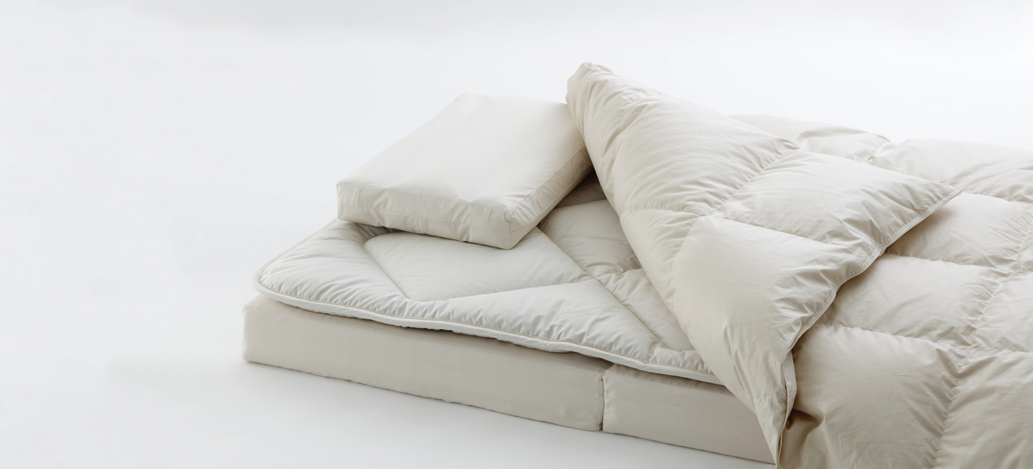 Cropped image of futon set by Iwata including floor pad, mattress pad, duvet, and pillow on a light gray background