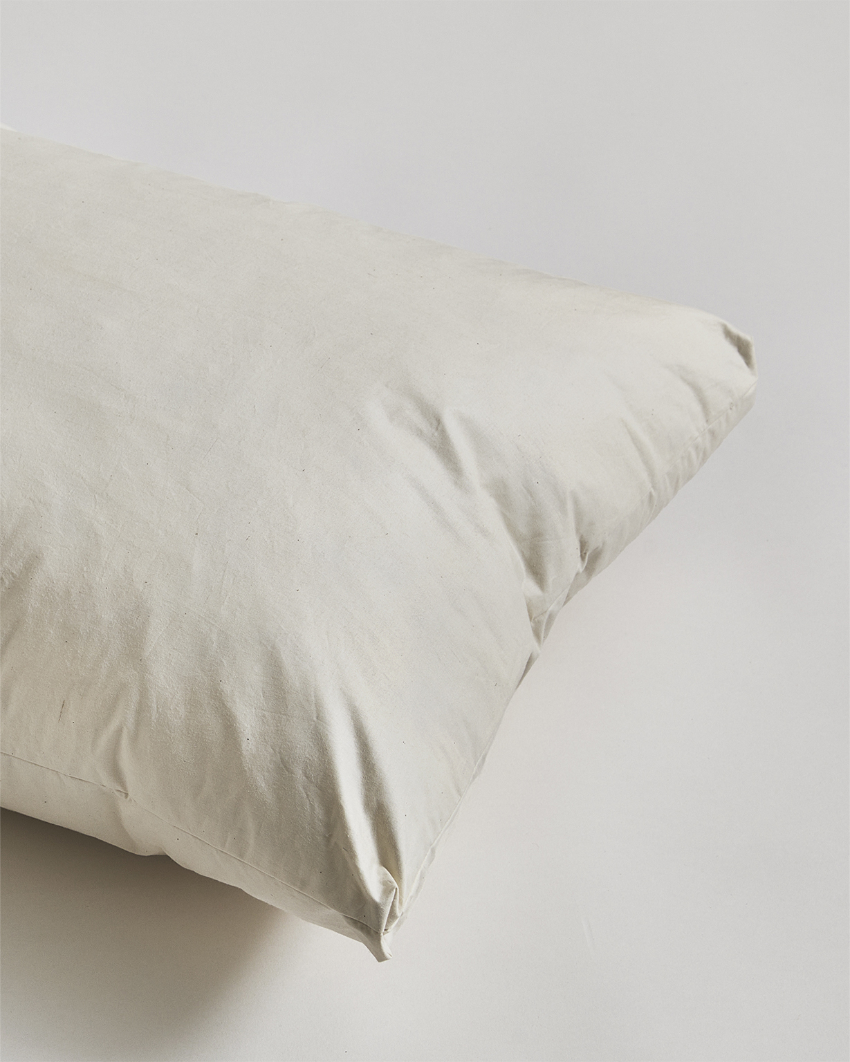 Up-close corner of down and feather pillow by Iwata on a gray background