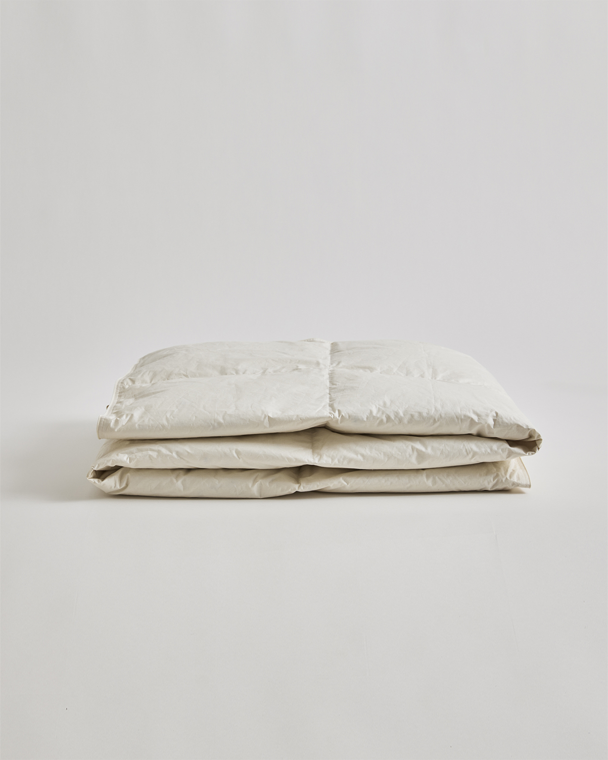 Folded unbleached duvet in light by Iwata on a gray background