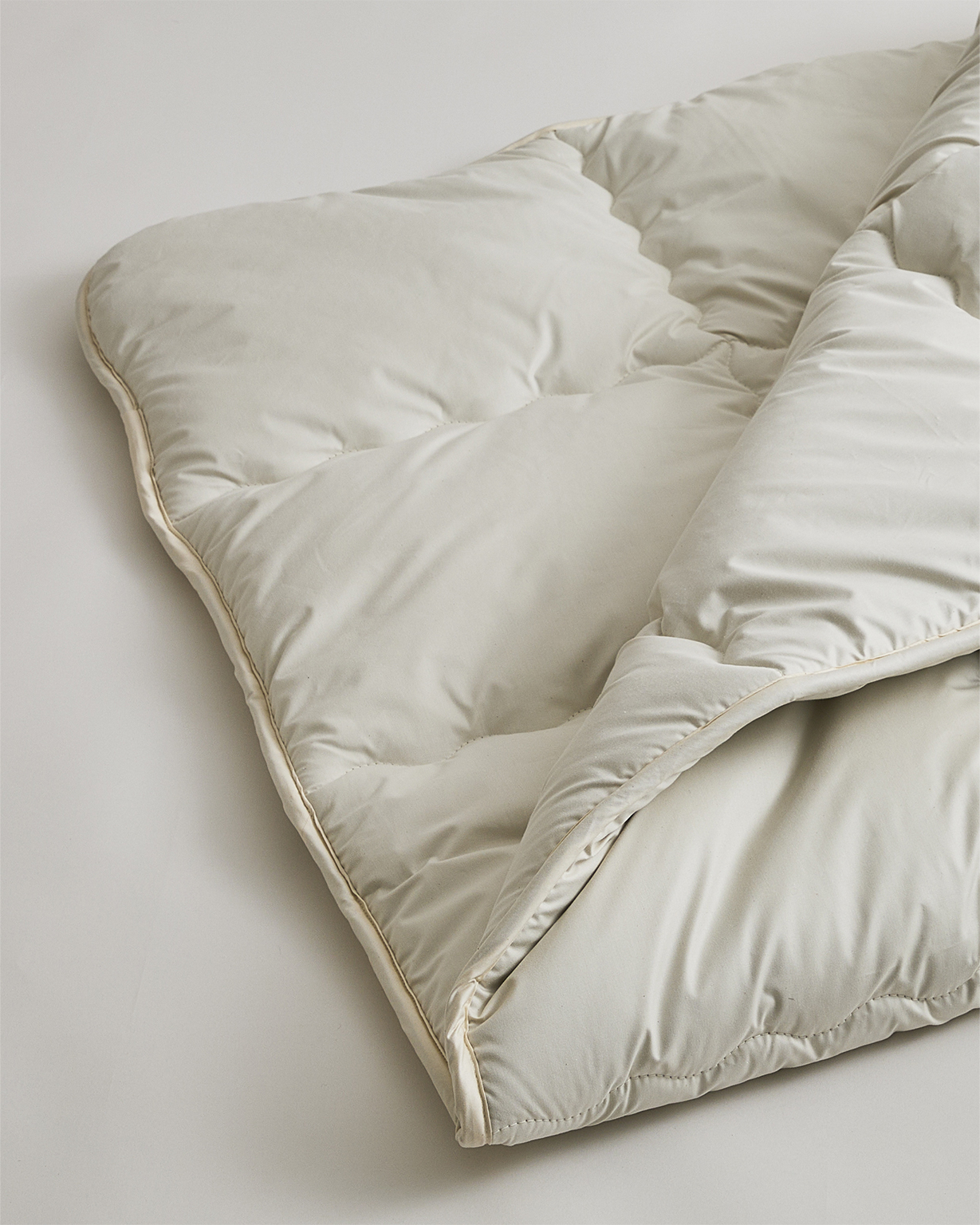 Up-close corner of camel hair mattress pad by Iwata on a gray background