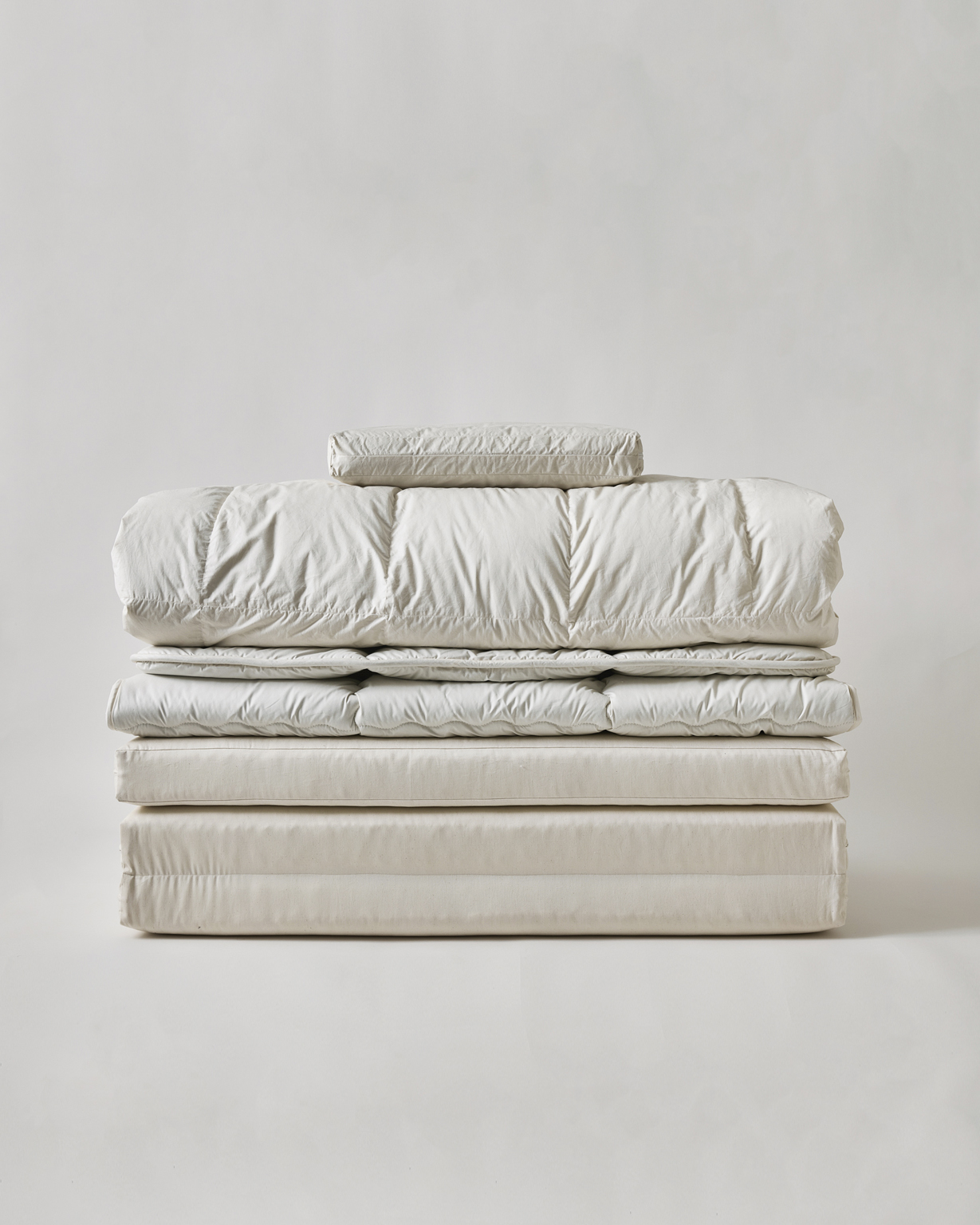 Folded futon set by Iwata including floor pad, mattress pad, duvet, and pillow on a light gray background