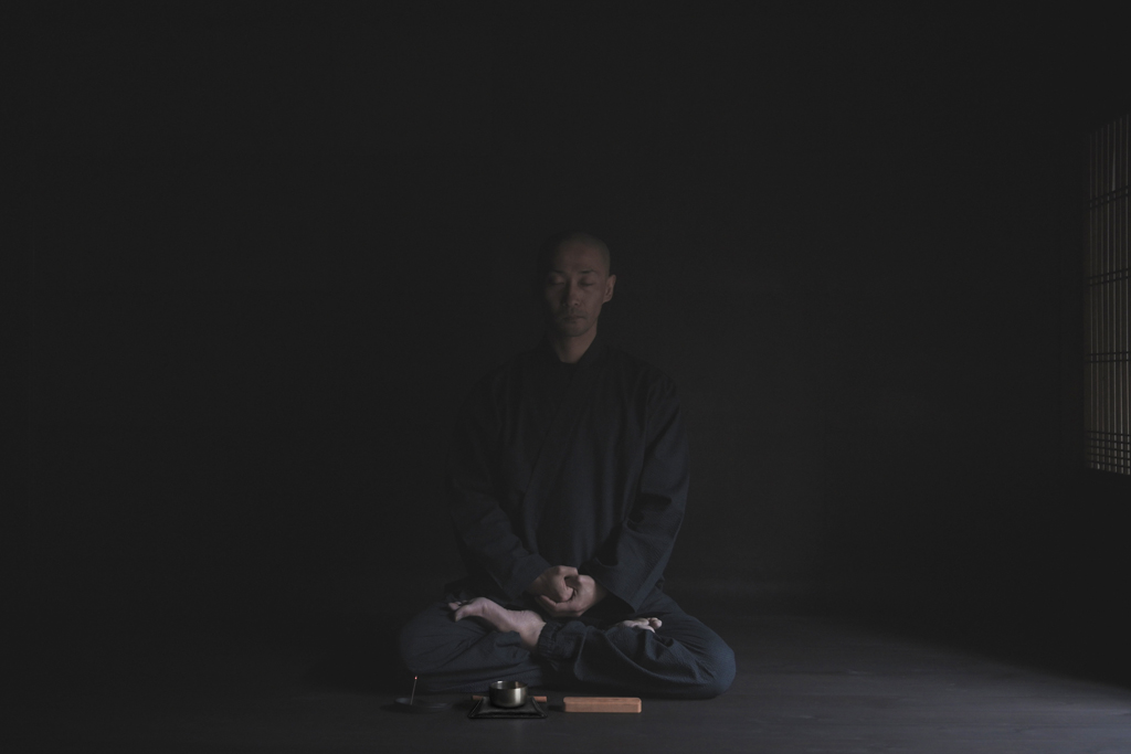 Monk sitting cross legged meditating in front of Nezen Boxed Items laid out in front of him